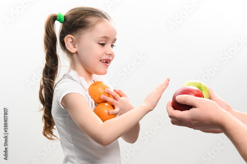 Portrait of a small beautiful girl on a white background with tangerines in her hands, who is also offered apples.