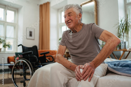 Portrait of senior man with knee pain sitting on a bed.