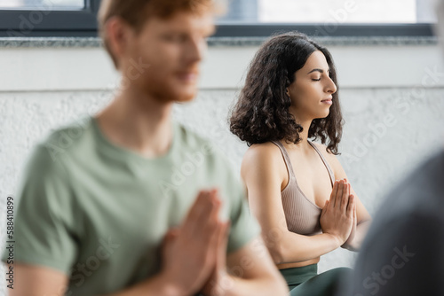 Middle eastern woman practicing anjali mudra in yoga group.