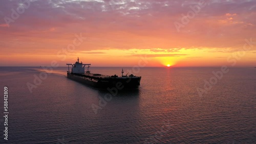 An elegant cargo ship gliding gently under the sun at sunset. A bulk carrier loaded with grains sailing from the open sea towards Bosphorus under a crimson sky. A bulker is a merchant ship specially  photo