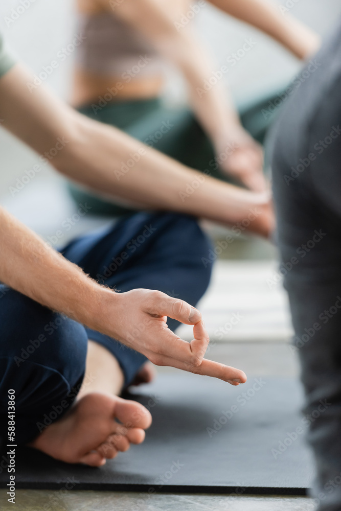 Cropped view of man doing gyan mudra on mat in yoga class.
