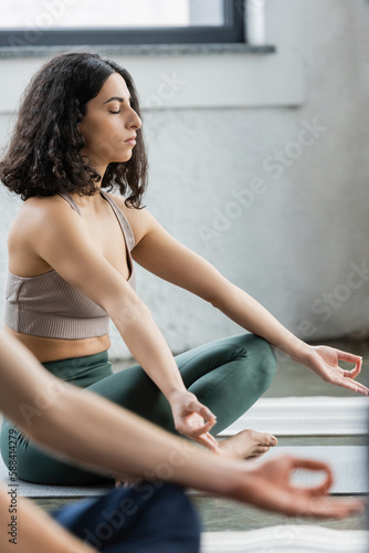 Middle eastern woman practicing gyan mudra on mat in yoga class.