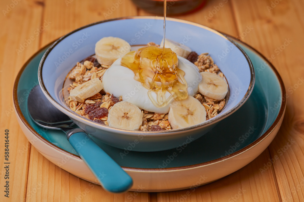 Bowl of granola with banana,yogurt with honey being drizzled over it. Bowl of granola with banana,yogurt with honey being drizzled over it.