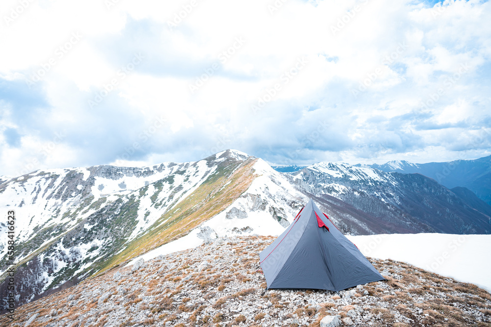 (Selective focus) Stunning view of a camping tent placed on the top of Monte Pratillo with snowcapped mountains in the distance, Prato di Campoli, Veroli, Frosinone, Italy.