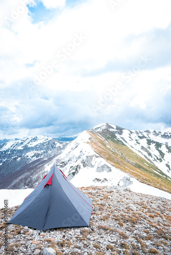 (Selective focus) Stunning view of a camping tent placed on the top of Monte Pratillo with snowcapped mountains in the distance, Prato di Campoli, Veroli, Frosinone, Italy.