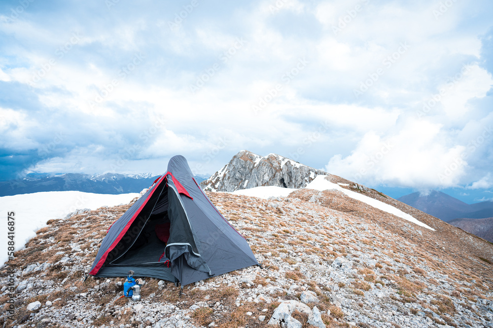 (Selective focus) Stunning view of a camping tent placed on the top of Monte Pratillo with snowcapped mountains in the distance, Prato di Campoli, Veroli, Frosinone, Italy.