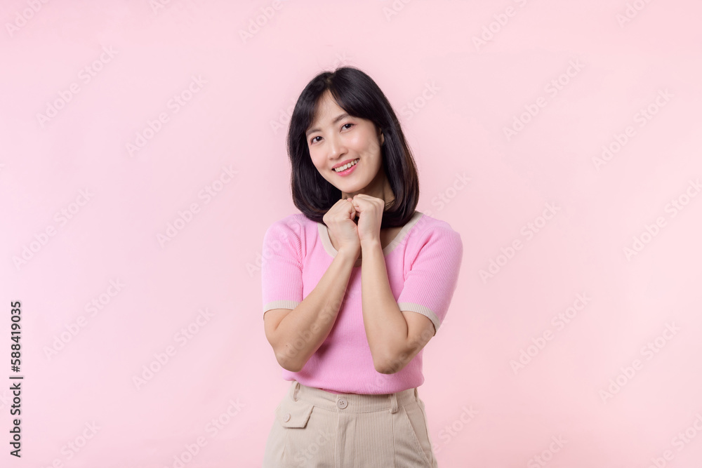 Adorable young happy asian woman model with shy emotion smiling expression cheerful positive attractive face and holding hand isolated on pink pastel studio background. Portrait beautiful cute lady. Adorable young happy asian woman model with shy emotion smiling expression cheerful positive attractive face and holding hand isolated on pink pastel studio background. Portrait beautiful cute lady.