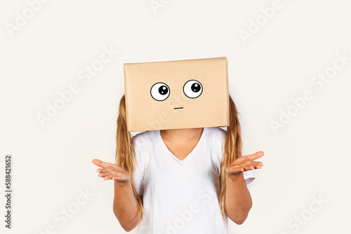 Mujer con caja de cartón en la cabeza con gesto de incertidumbre y con las manos levantadas sobre un fondo blanco liso y aislado. Vista de frente y de cerca. Copy space