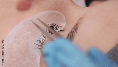Eyelash extension procedure. The working process of professional beauty master lengthening female lashes. Fake eyelashes. Eyelashes extensions close up. Makeup artist and client in beauty salon. photo