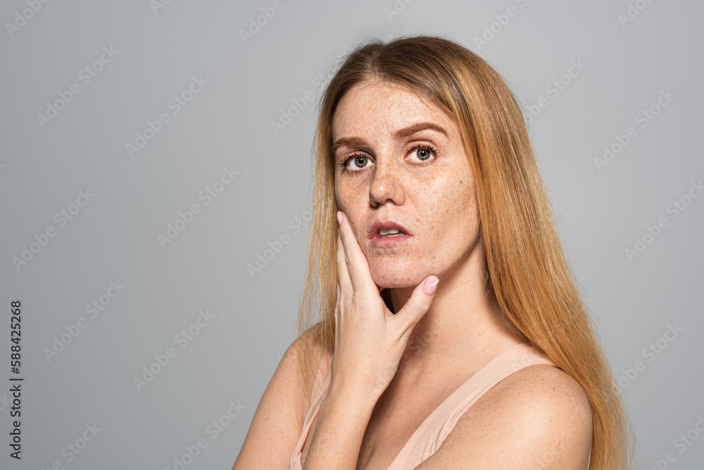 Young woman with freckles on face touching skin isolated on grey. Young woman with freckles on face touching skin isolated on grey.