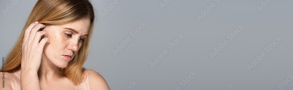 Displeased woman with freckles on face looking down isolated on grey, banner. Displeased woman with freckles on face looking down isolated on grey, banner.
