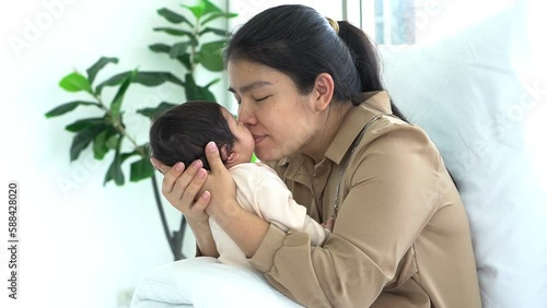 an Asian mother kissing mouth her 1-month-old baby newborn girl, with happy and love, concept to Asian family and baby newborn photo