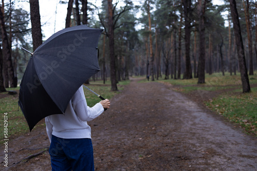 Rainy season. girl holding black umbrella walking in a forest park in a rain. Outdoor activity and enjoy nature in any weather conditions.