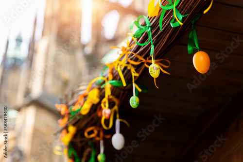 Sticker Multicolored bright easter eggs decoration hanged on paper ribbons on wooden house roof against old cathedral church in historical center european city market square