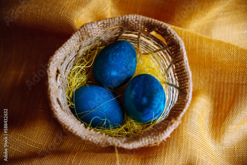 Three blue dyed easter eggs in the basket on the golden textured background. Central composition