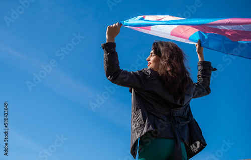 Quadro su tela Transgender woman raising the trans flag in flight with a clear sky in the background