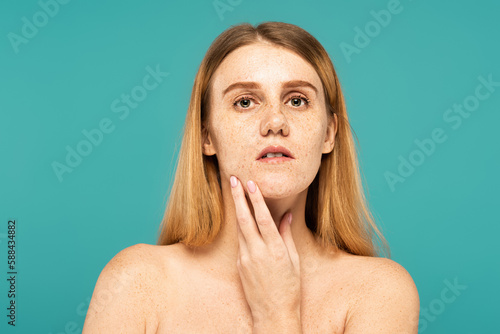 Young woman with freckles and naked shoulders looking at camera isolated on turquoise.