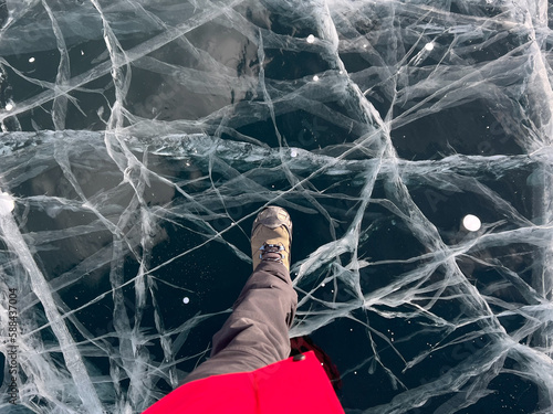 A foot of tourist standing on the cracks surface of frozen lake Baikal in the winter season of Siberia, Russia