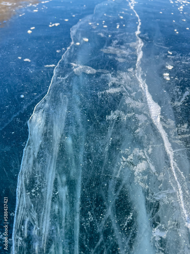 The natural texture of winter ice with white bubbles and cracks on a frozen lake. Abstract background of ice and cracks on the surface of frozen Lake Baikal