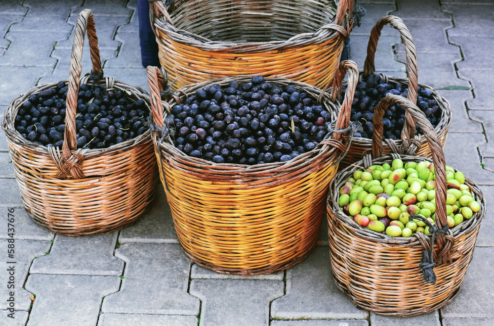 Wicker baskets full of green and black olives standing outdoor on paving stones. Street food market in Turkey.