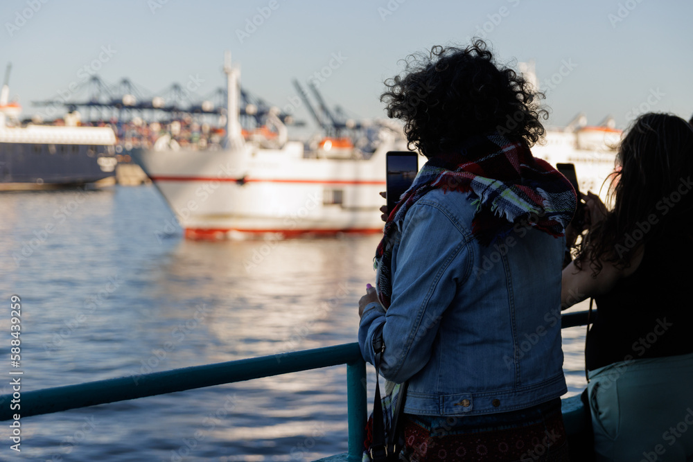 Woman on a ferry photographing other boats and the port