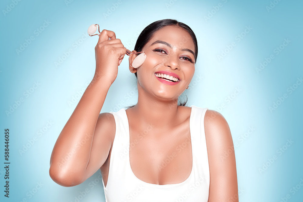 Young aesthetic Asian woman using natural rose quartz spa product to relax on blue background. Skin care, face roller and beauty woman with facial massage for dermatology, cosmetic and wellness. Young aesthetic Asian woman using natural rose quartz spa product to relax on blue background. Skin care, face roller and beauty woman with facial massage for dermatology, cosmetic and wellness.