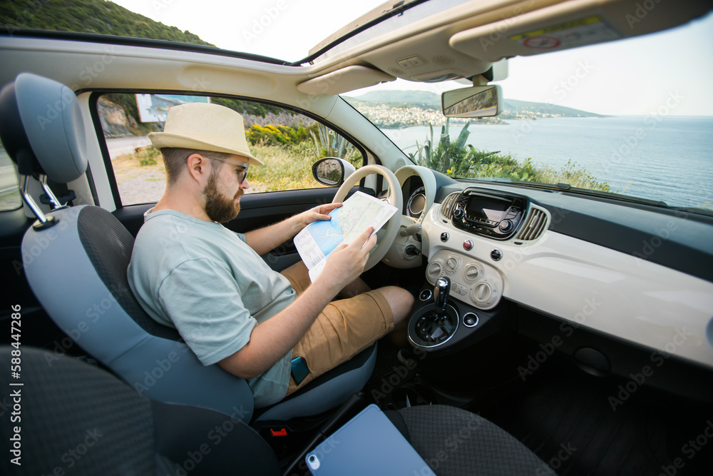 Hipster man looking on location navigation map in car, tourist traveler driving and hold in male hands europe cartography, view and plan tourist way road, trip in transportation cabriolet auto