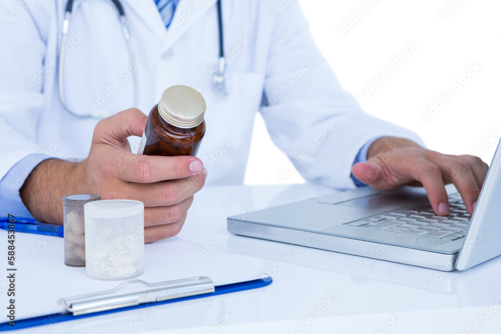 Midsection of doctor holding medicine bottle while using laptop Midsection of doctor holding medicine bottle while using laptop