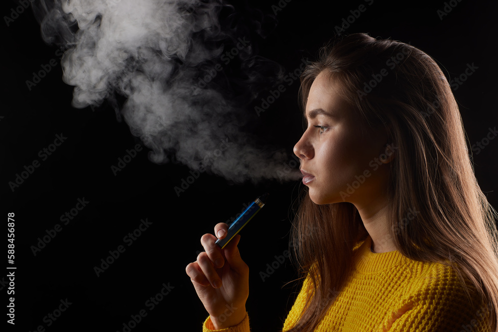 Obraz premium young girl smokes a vape close-up on a dark background