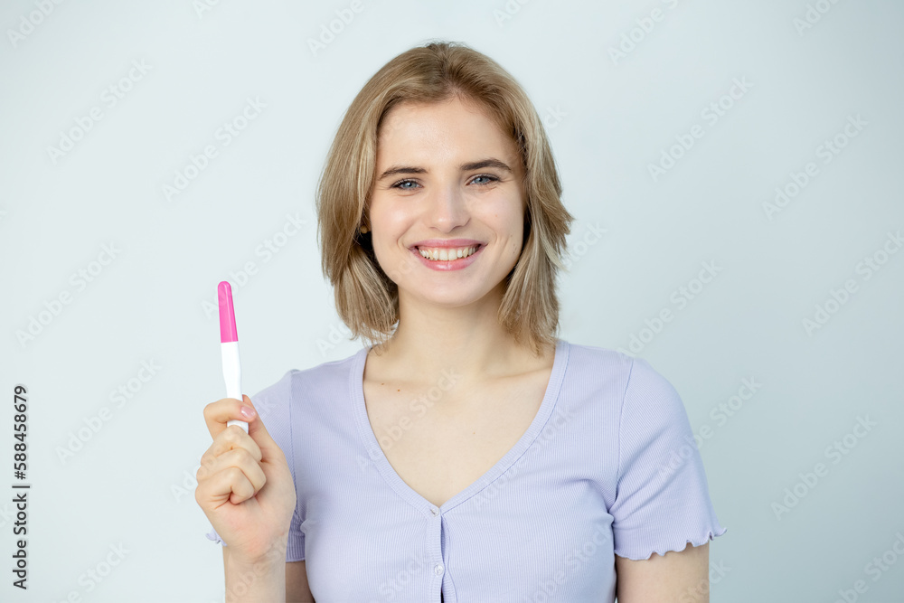 Happy caucasian young woman holding pregnancy test and smilind friendly, close up. Woman looks at pregnancy ovulation test celebrate positive result get pregnan. IVF concept Happy caucasian young woman holding pregnancy test and smilind friendly, close up. Woman looks at pregnancy ovulation test celebrate positive result get pregnan. IVF concept