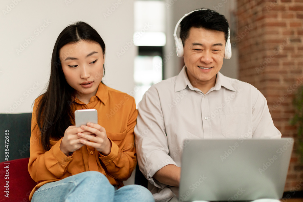 Young asian wife spying on husband with laptop, woman caught man texting with mistress, sitting next to each other Young asian wife spying on husband with laptop, woman caught man texting with mistress, sitting next to each other