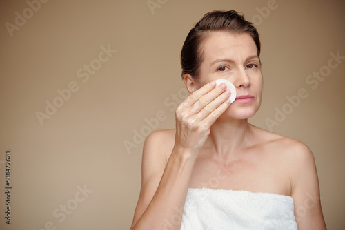 Mature woman wiping off make-up with cotton pad soaked in micelar water photo