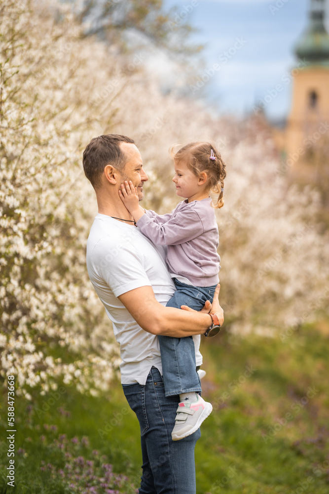 Fototapeta premium Father and daughter having a fun together under a blooming tree in spring park Petrin in Prague, Europe
