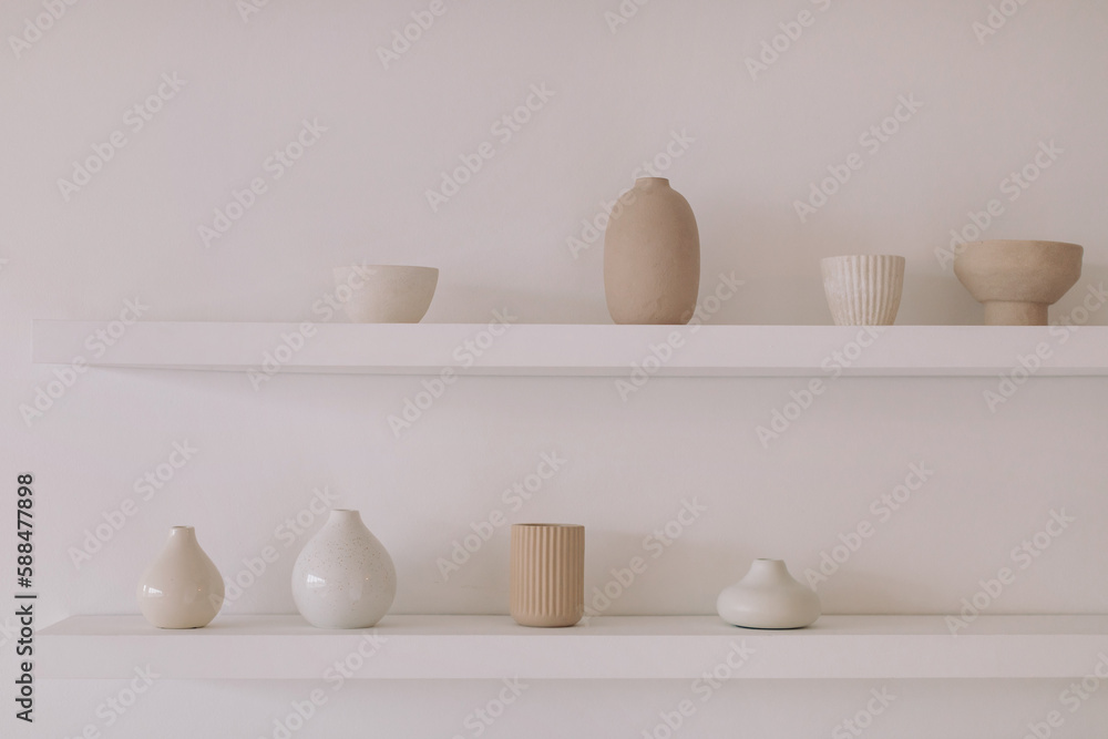 Ceramic products of different shapes on a shelf on a white wall. Aesthetic home decor. Minimalistic background. Ceramic products of different shapes on a shelf on a white wall. Aesthetic home decor. Minimalistic background.