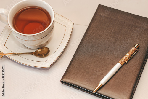 White cup and saucer with golden spoon and notepad.