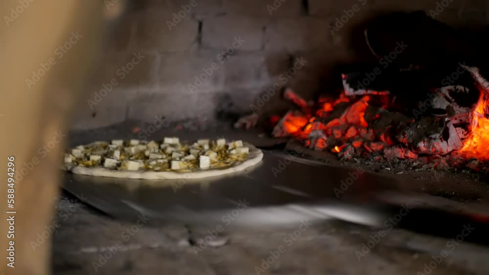 A baker placed a raw pizza with cheese chunks in a professional charcoal stone oven using an aluminum pizza spatula. cooking real pizza in an italian bakery. A baker placed a raw pizza with cheese chunks in a professional charcoal stone oven using an aluminum pizza spatula. cooking real pizza in an italian bakery.
