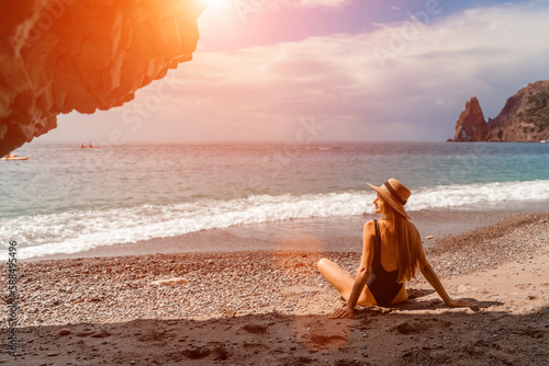 View of a woman in a black swimsuit from a sea cave Attractive woman enjoying the sea air sits on the beach and looks at the sea.