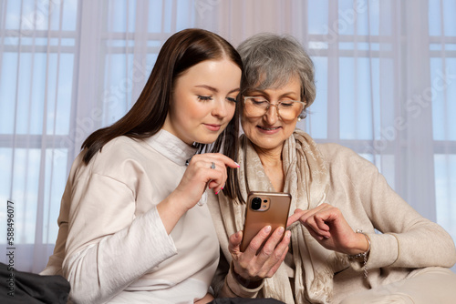 A young girl is explaining to an elderly woman how to use a phone. The granddaughter is showing her phone to her grandmother. a family pastime, helping and respecting the elderly.