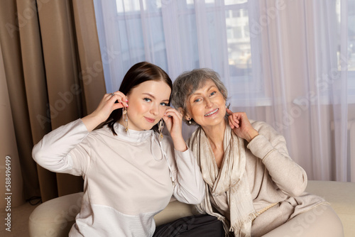 A grandmother or elderly woman is trying on and giving her earrings, jewelry to her granddaughter or a young girl. Family tradition, Passing down memories.