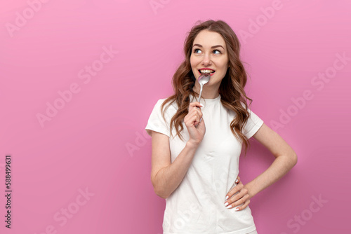 Fotografie, Obraz hungry woman licks spoon and dreams on pink isolated background, pensive girl in