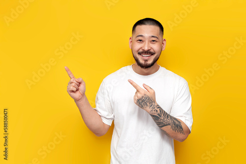 Quadro em tela adult tattooed asian man in white t-shirt shows his hands to the side on yellow