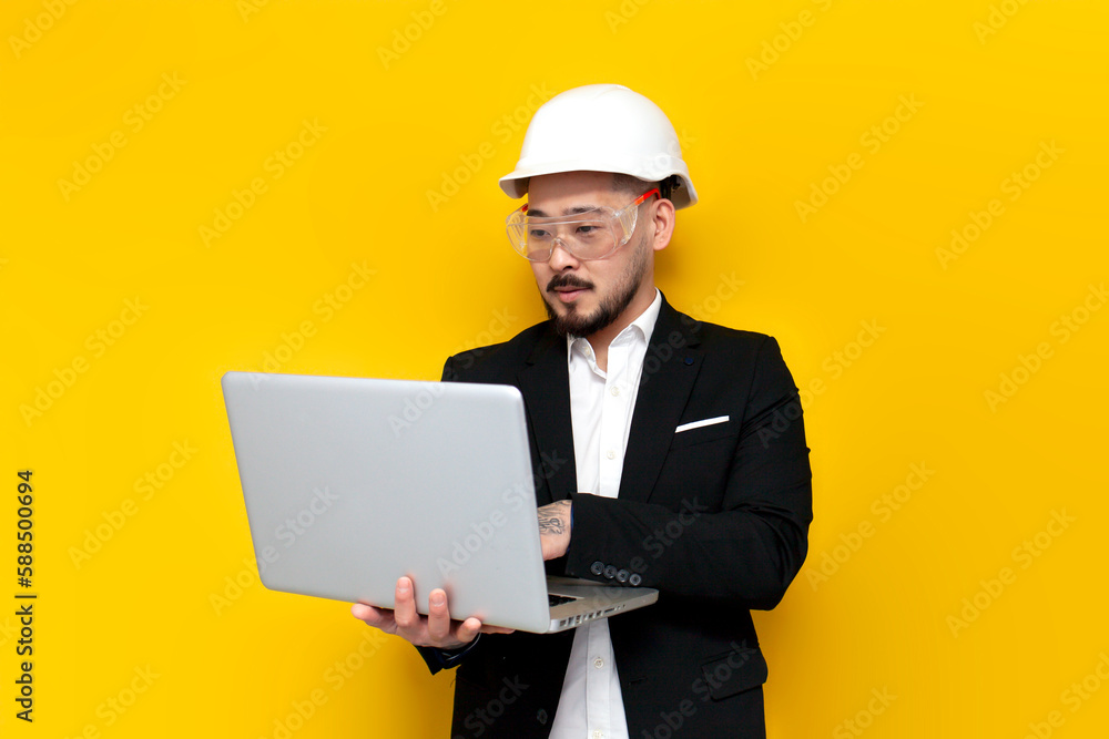 asian foreman in black suit uses laptop on yellow isolated background, korean civil engineer in hard hat and glasses asian foreman in black suit uses laptop on yellow isolated background, korean civil engineer in hard hat and glasses