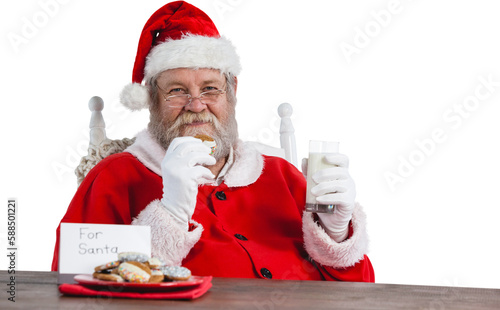 Santa Claus holding glass of milk and cookie by table