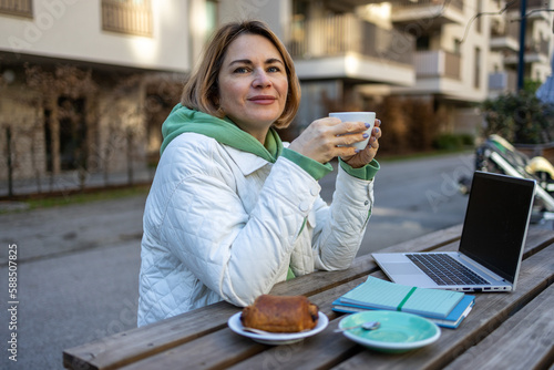 Middle aged matured smiling blond woman drinking a coffee in the street cafe