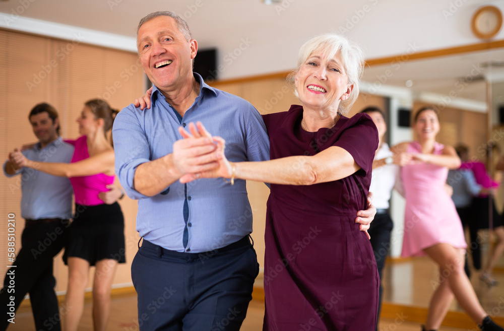 Fototapeta premium Dynamic aged pair engaging in Latino dance in dance studio. Pairs training ballroom dance in hall