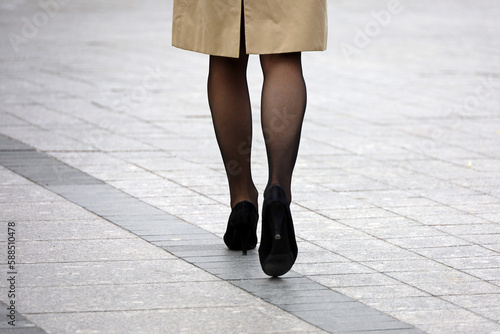 Slim woman in coat, black stockings and shoes on high heels walking down the street, female fashion in spring city