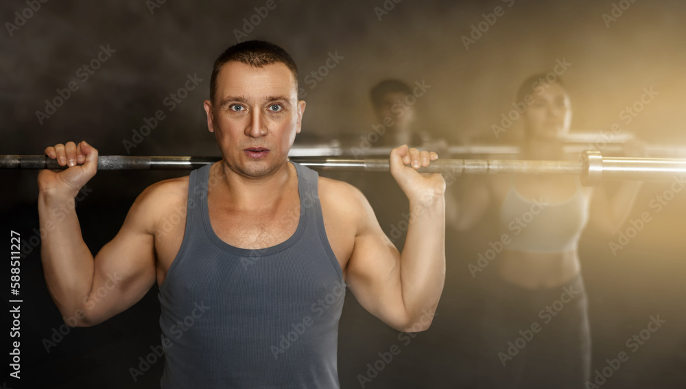 Portrait of sporty man doing exercises with barbell to strengthen body muscles in modern gym during group workout. Physical activity and bodybuilding concept..