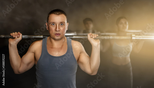 Portrait of sporty man doing exercises with barbell to strengthen body muscles in modern gym during group workout. Physical activity and bodybuilding concept..
