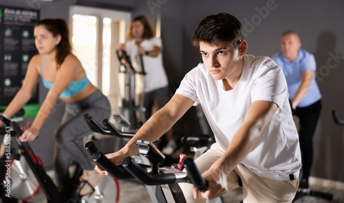 Portrait of concentrated young guy doing cardio training, cycling on stationary bike in gym. Sport and fitness concept
