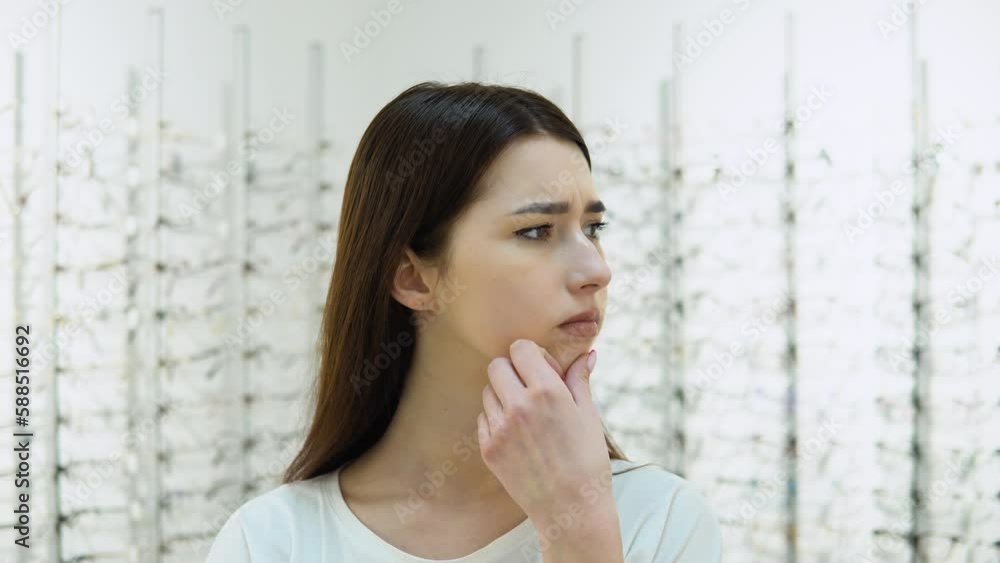 Conceived young woman choosing glasses at optics store. Excited upset girl cannot choose glasses in the store Conceived young woman choosing glasses at optics store. Excited upset girl cannot choose glasses in the store